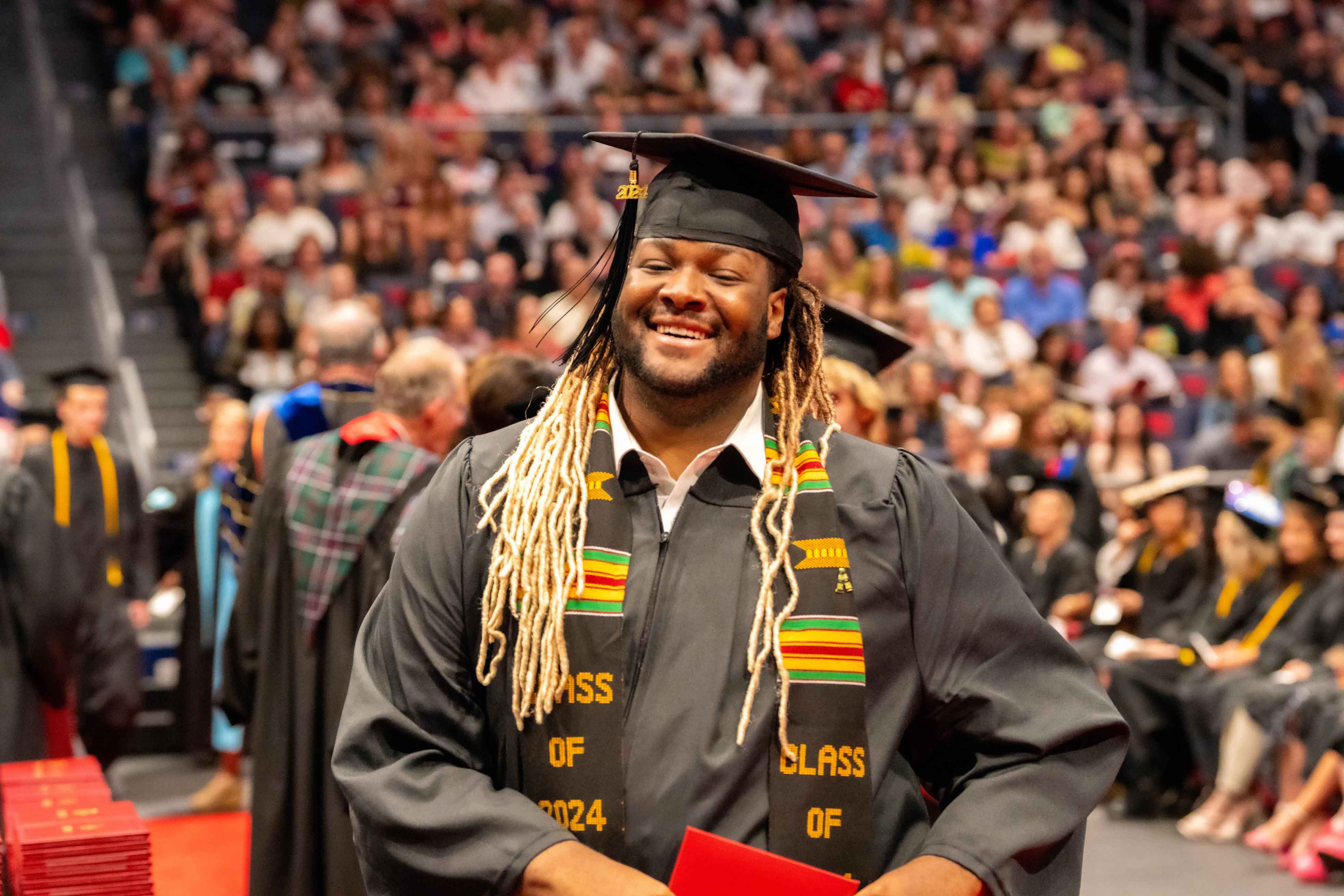 A smiling Sinclair graduate proudly displays their diploma at a commencement ceremony.