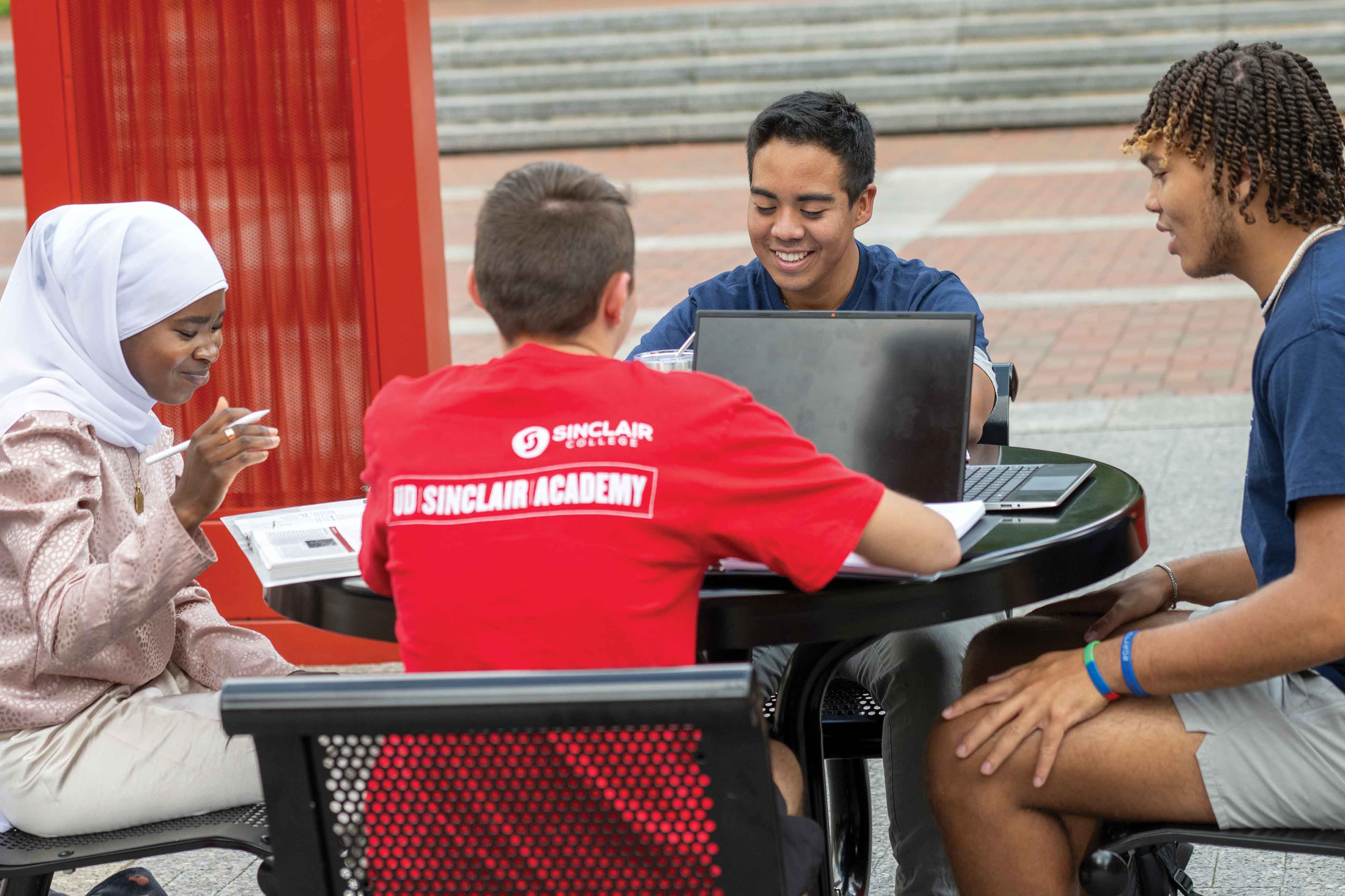A diverse group of students studying and collaborating at an outdoor table.